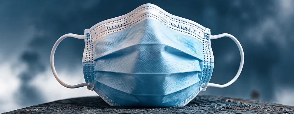 Blue disposable face mask lying on rough ground with a stormy, cloudy sky in the background.